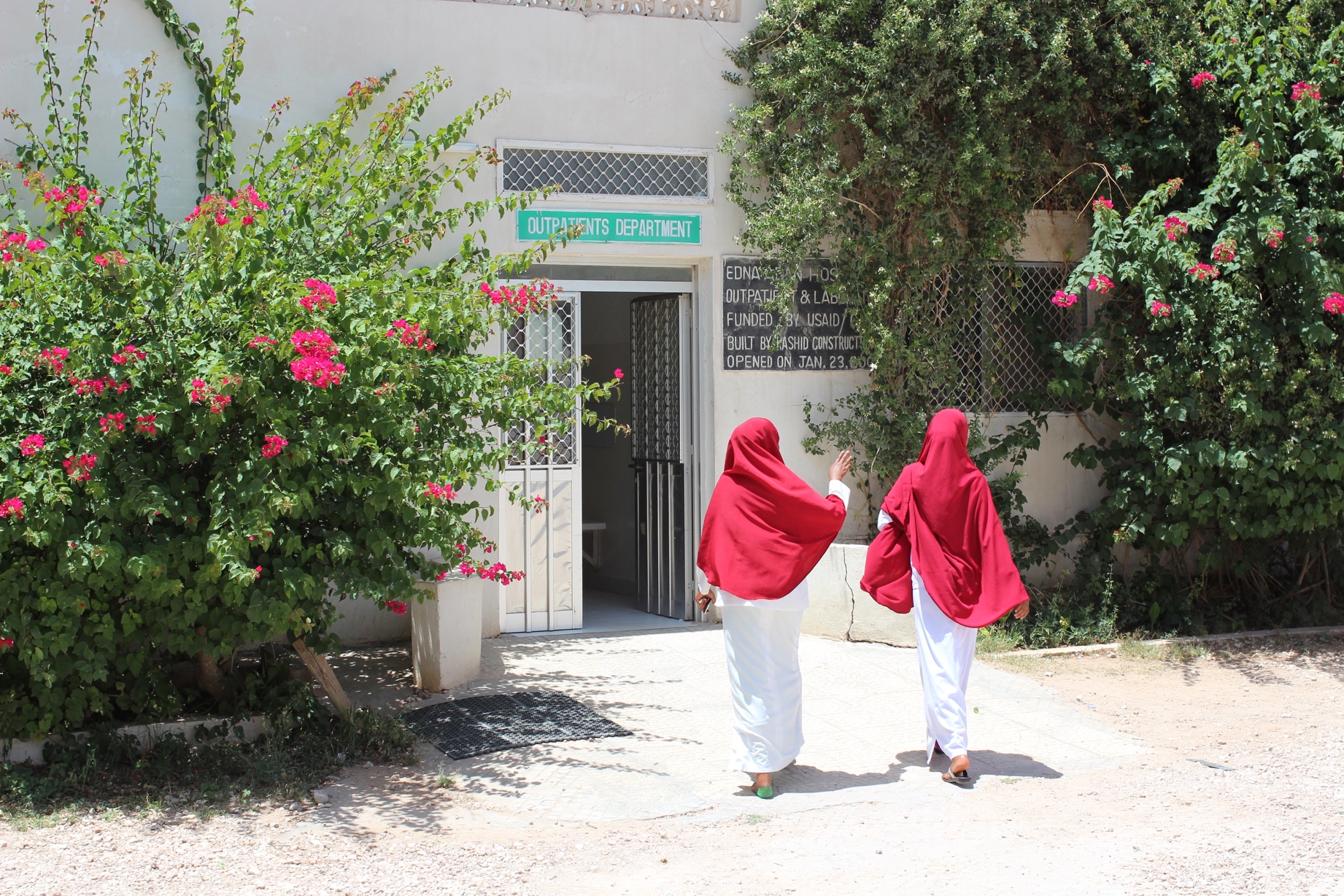 Two people in white uniforms and red headscarves walking into the outpatient department at Edna Adan Hospital.